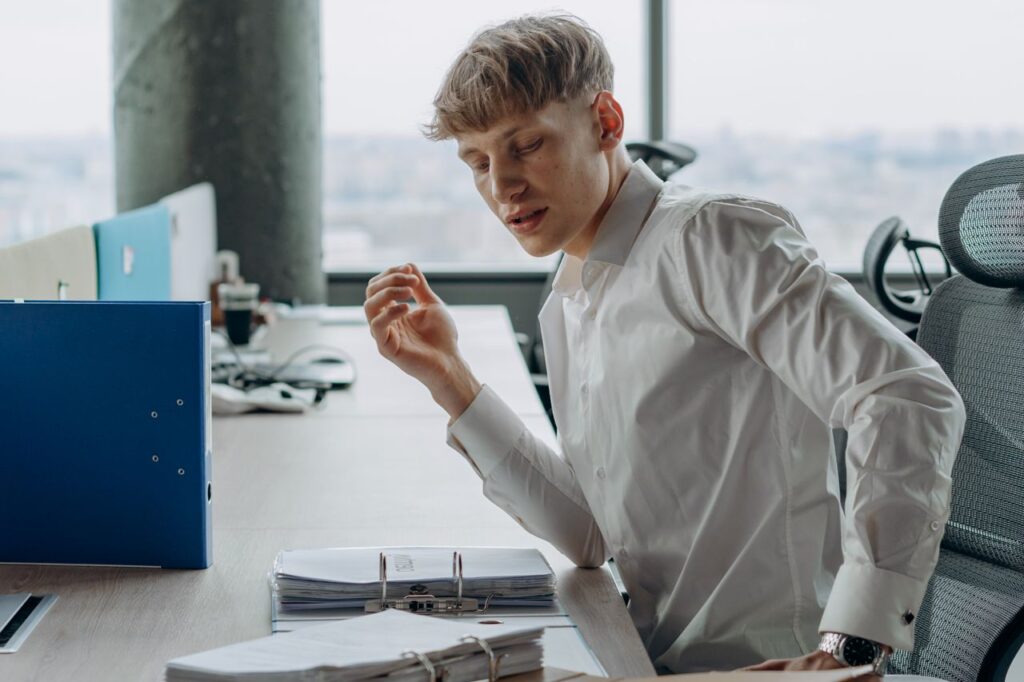 Man in white shirt sitting at office desk reading documents, modern workspace.